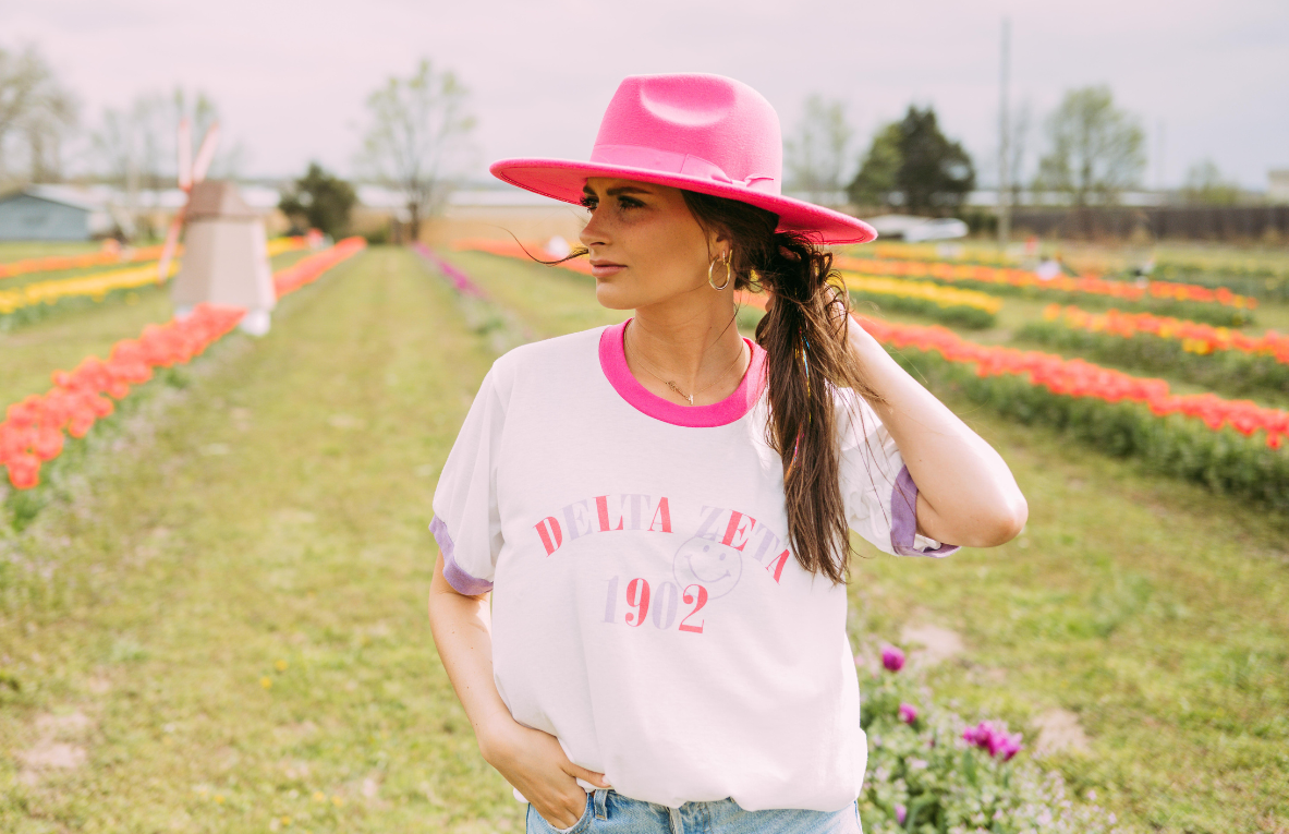A girl wears a white color block ringer that reads Delta Zeta 1902