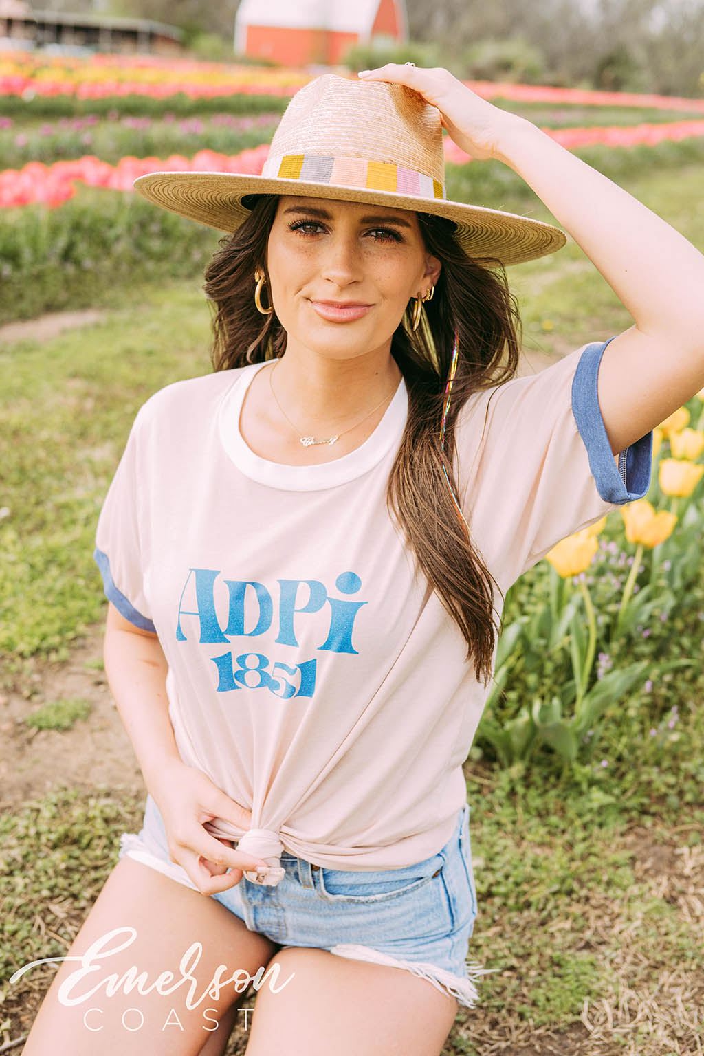Girl sits in tulip field wearing a white ADPi 1851 ringer tshirt.