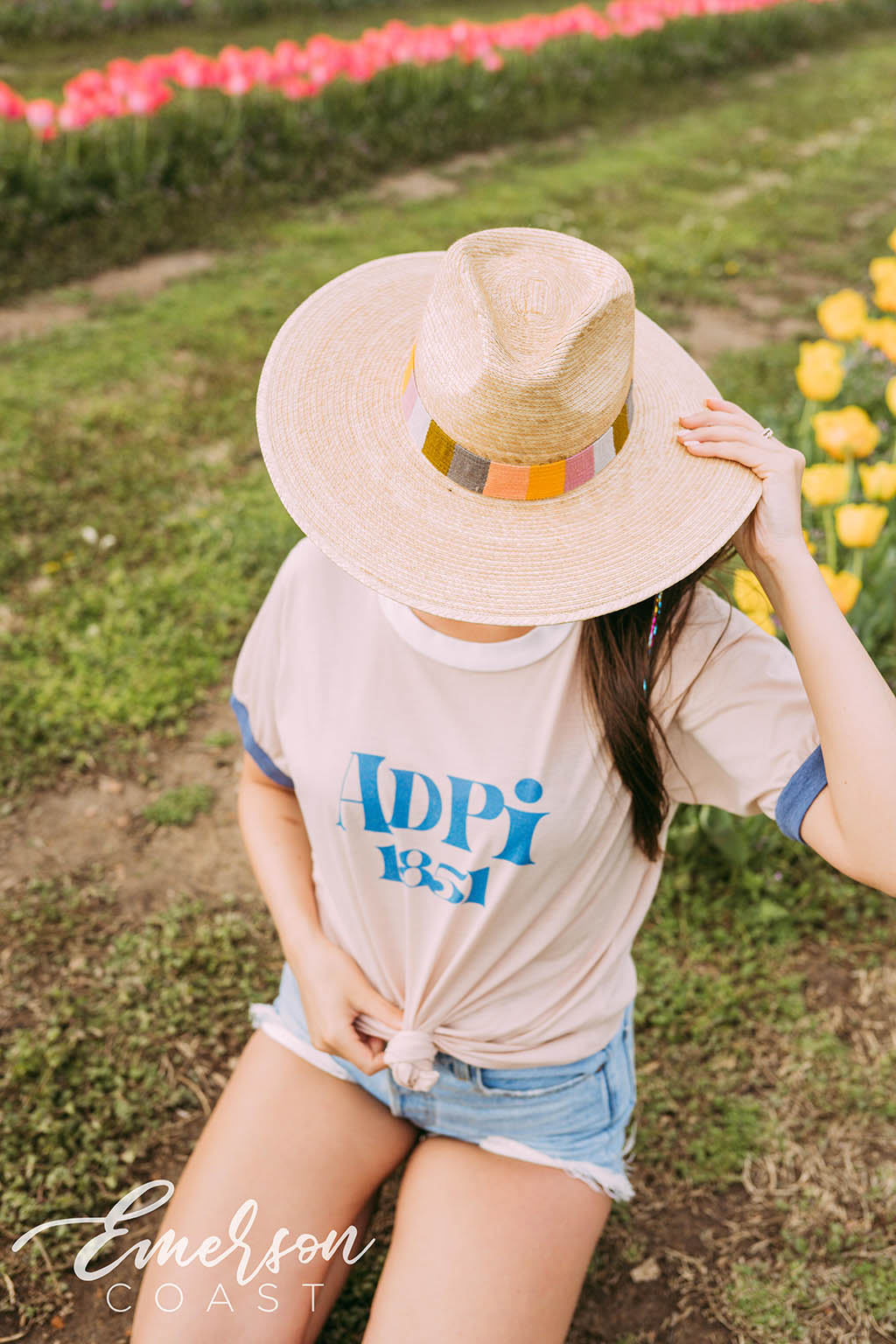 Girl sits in tulip field wearing a white ADPi 1851 ringer tshirt.