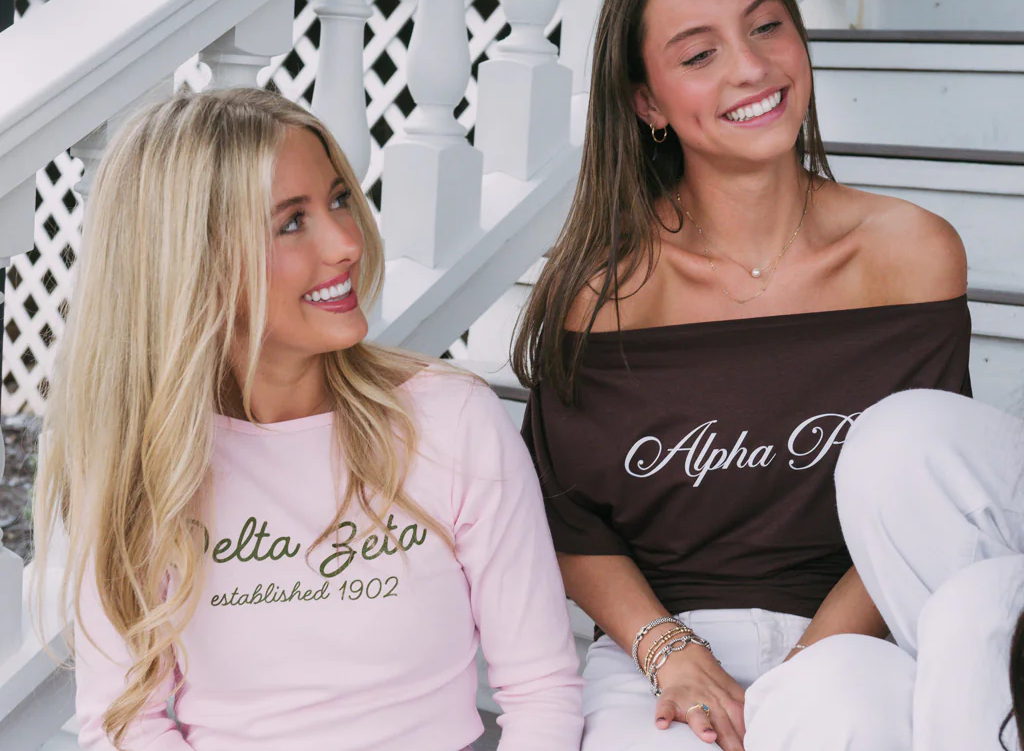 Two women on porch steps wearing pink Delta Zeta established 1902 top and brown off-shoulder Alpha Phi top