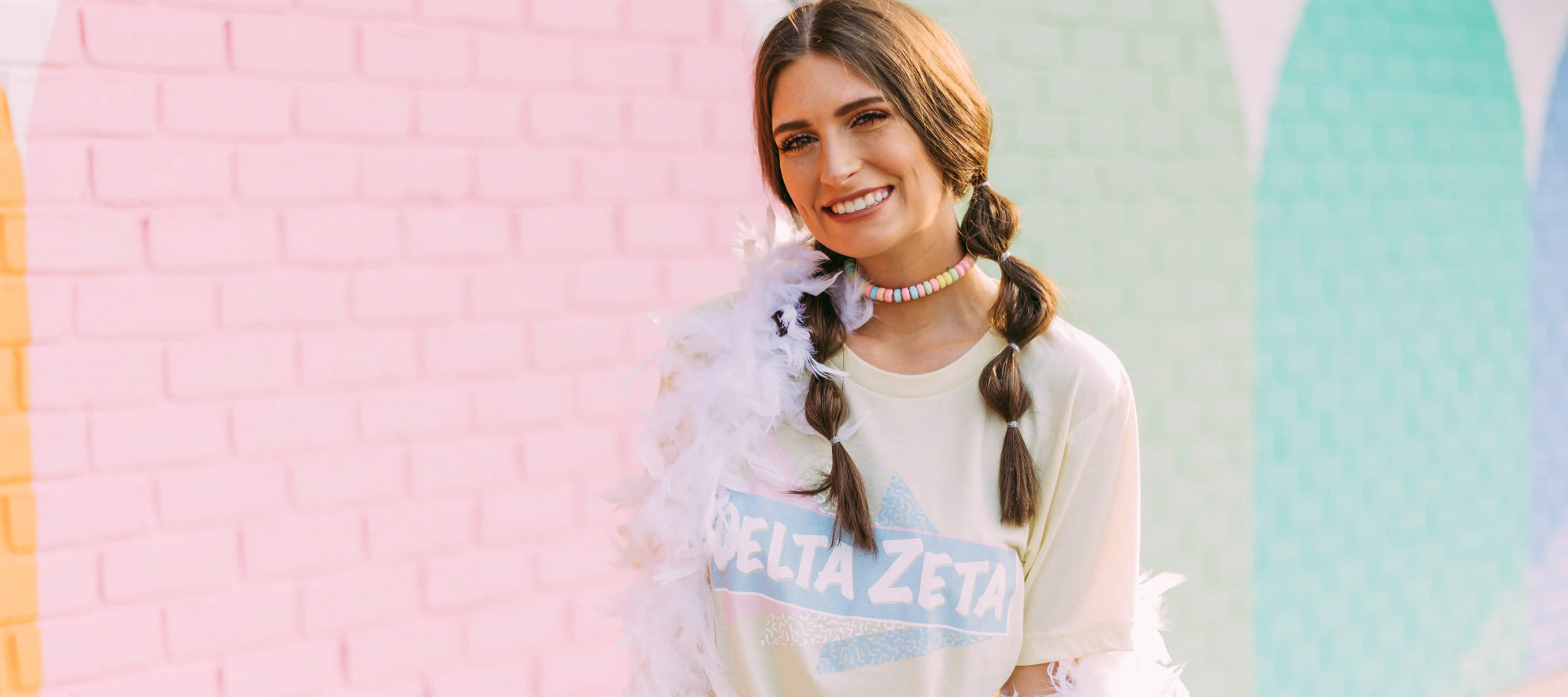 Girl stands in front of a colorful wall wearing a Delta Zeta tshirt