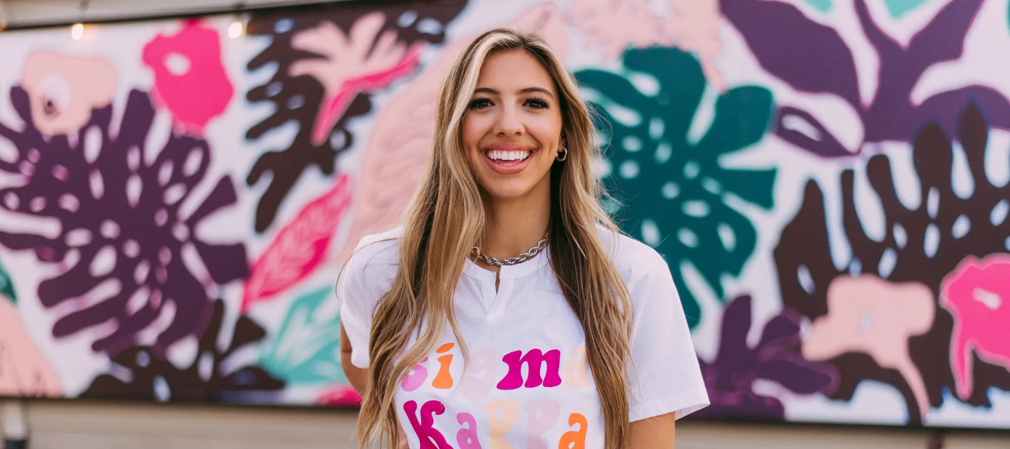 Girl wears a white Sigma Kappa tshirt with colorful letters
