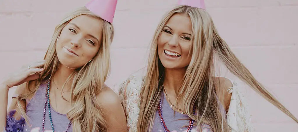 Two girls wear purple tank tops and party hats