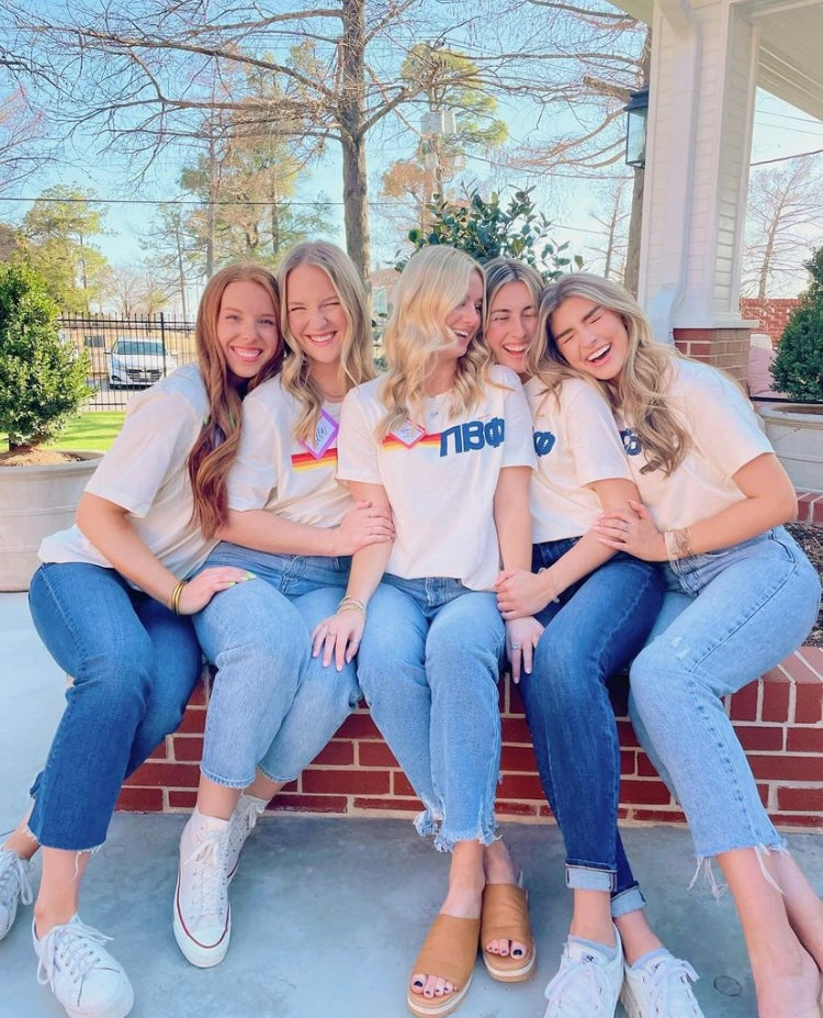 Five girls sit together wearing cream colored Pi Phi Tshirts