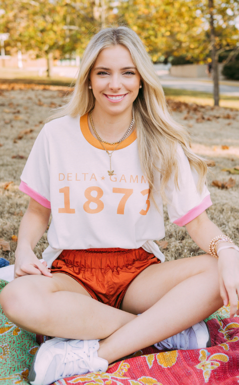 Girl sits wearing white Delta Gamma ringer tshirt