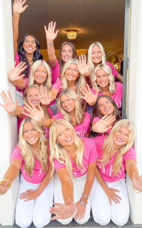 Women sit in a door stack in a doorway wearing pink shirts and white jeans