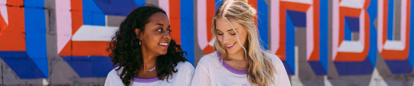 Two girls sit together wearing white shirts with purple necklines.