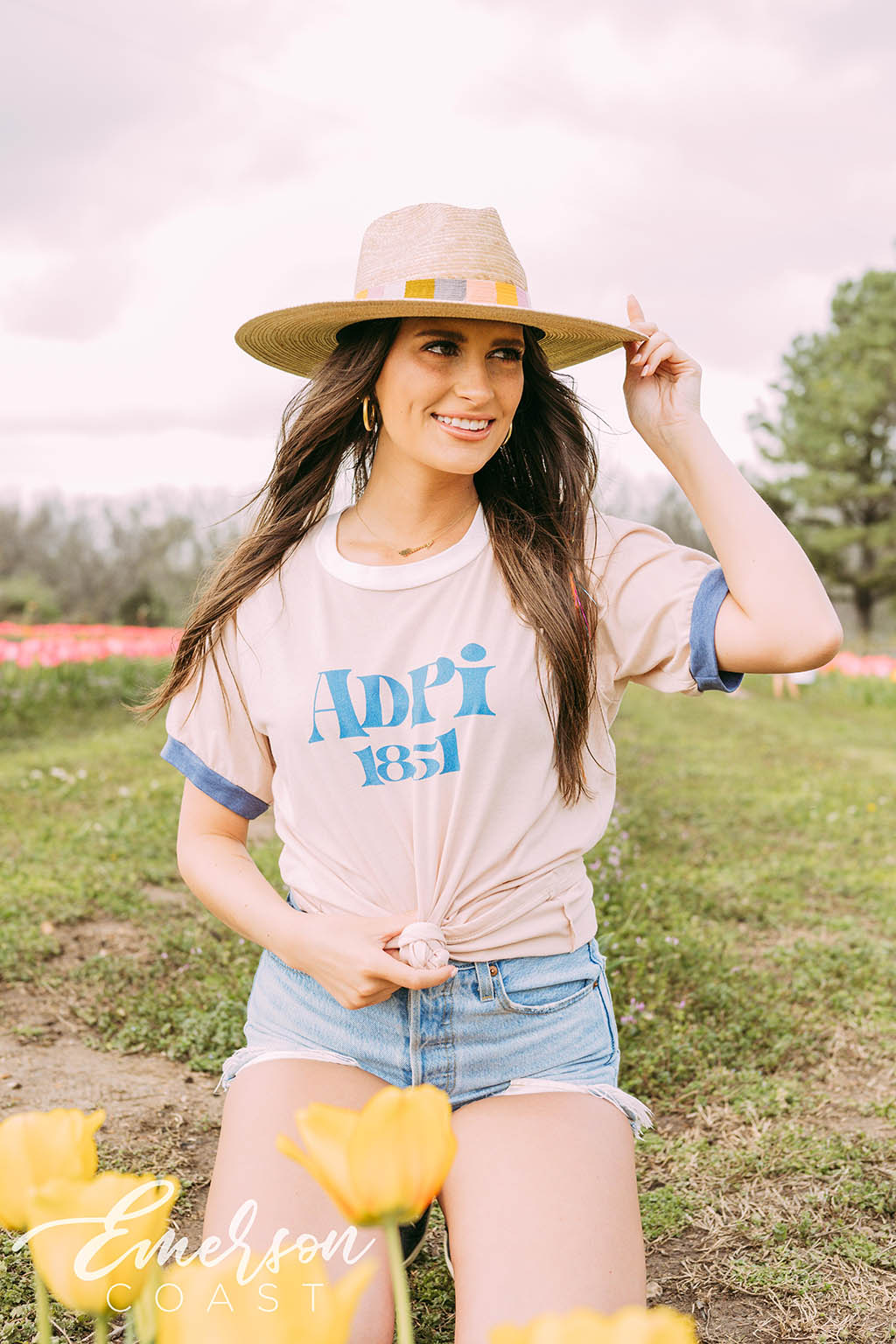 Girl sits in tulip field wearing a white ADPi 1851 ringer tshirt.