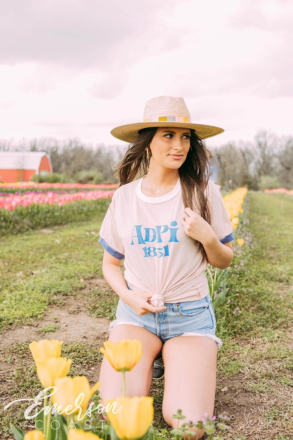 Girl sits in tulip field wearing a white ADPi 1851 ringer tshirt.