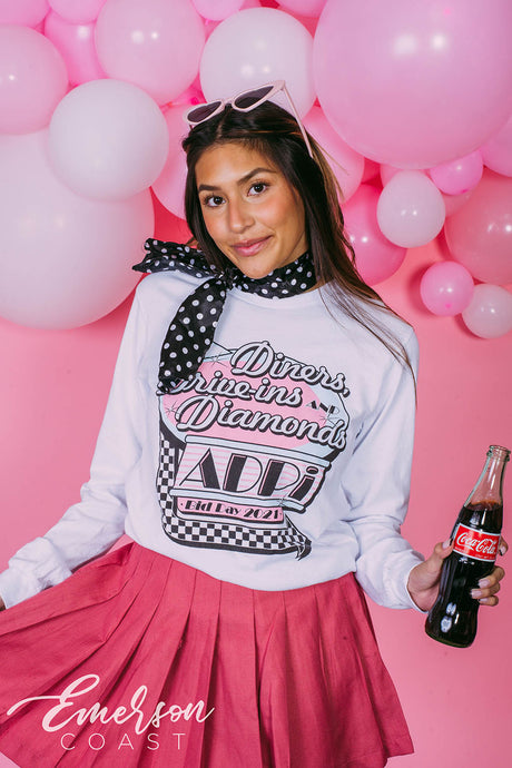Girl wears white long sleeve that reads "Diners, Drive-ins, and Diamonds. ADPi Bid Day."