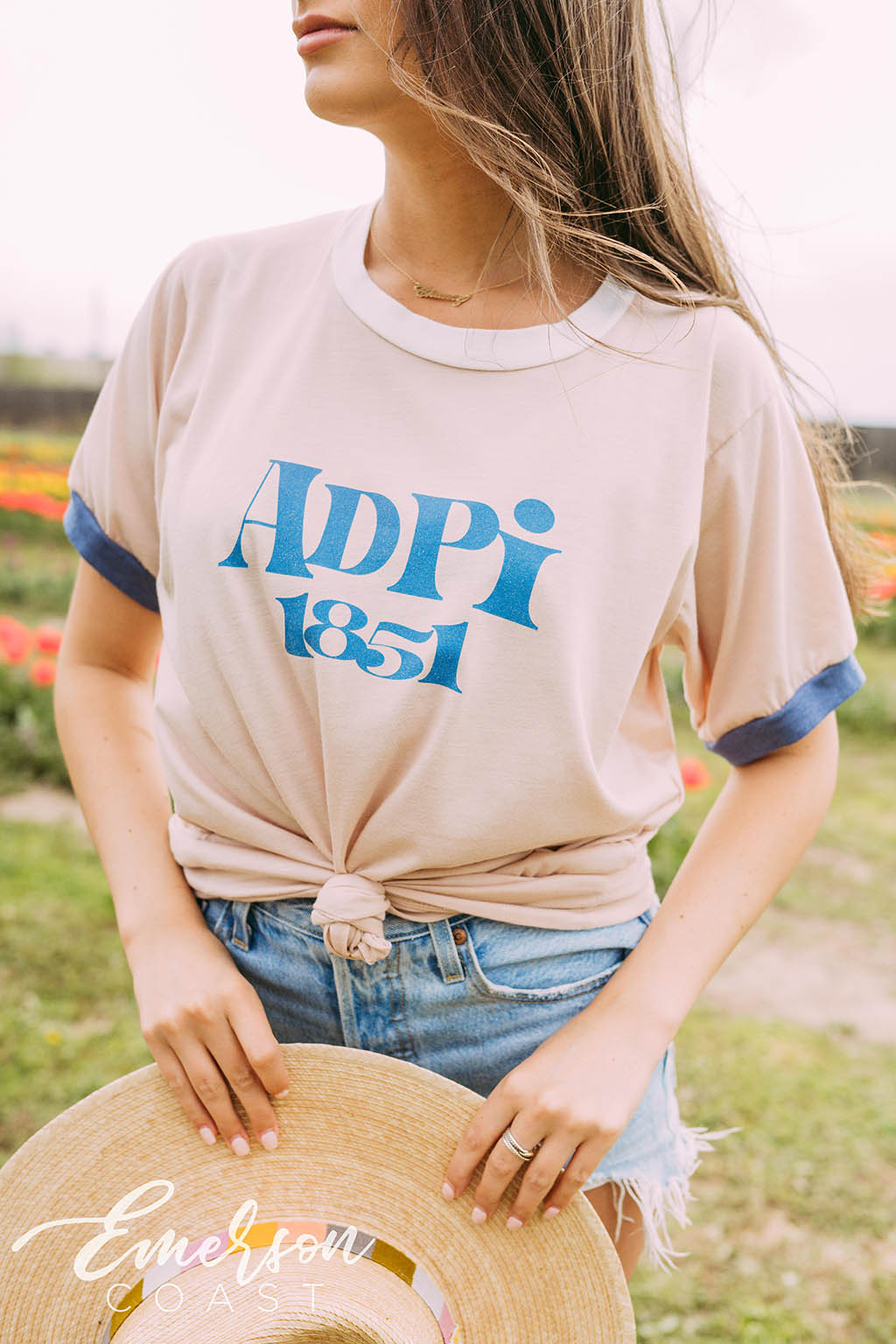 Girl sits in tulip field wearing a white ADPi 1851 ringer tshirt.