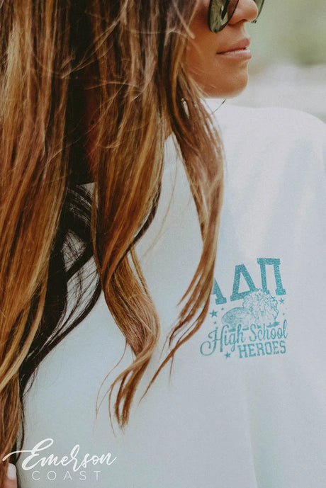 Girl wears a light blue shirt that has ADPi letters  and "High School Heroes" on the left chest