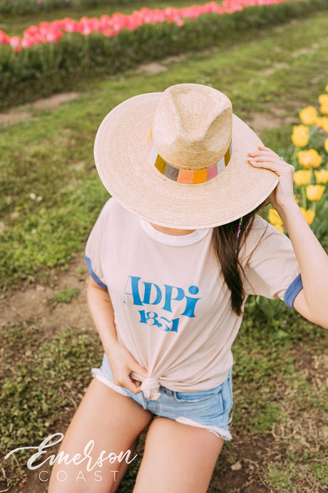 Girl sits in tulip field wearing a white ADPi 1851 ringer tshirt.