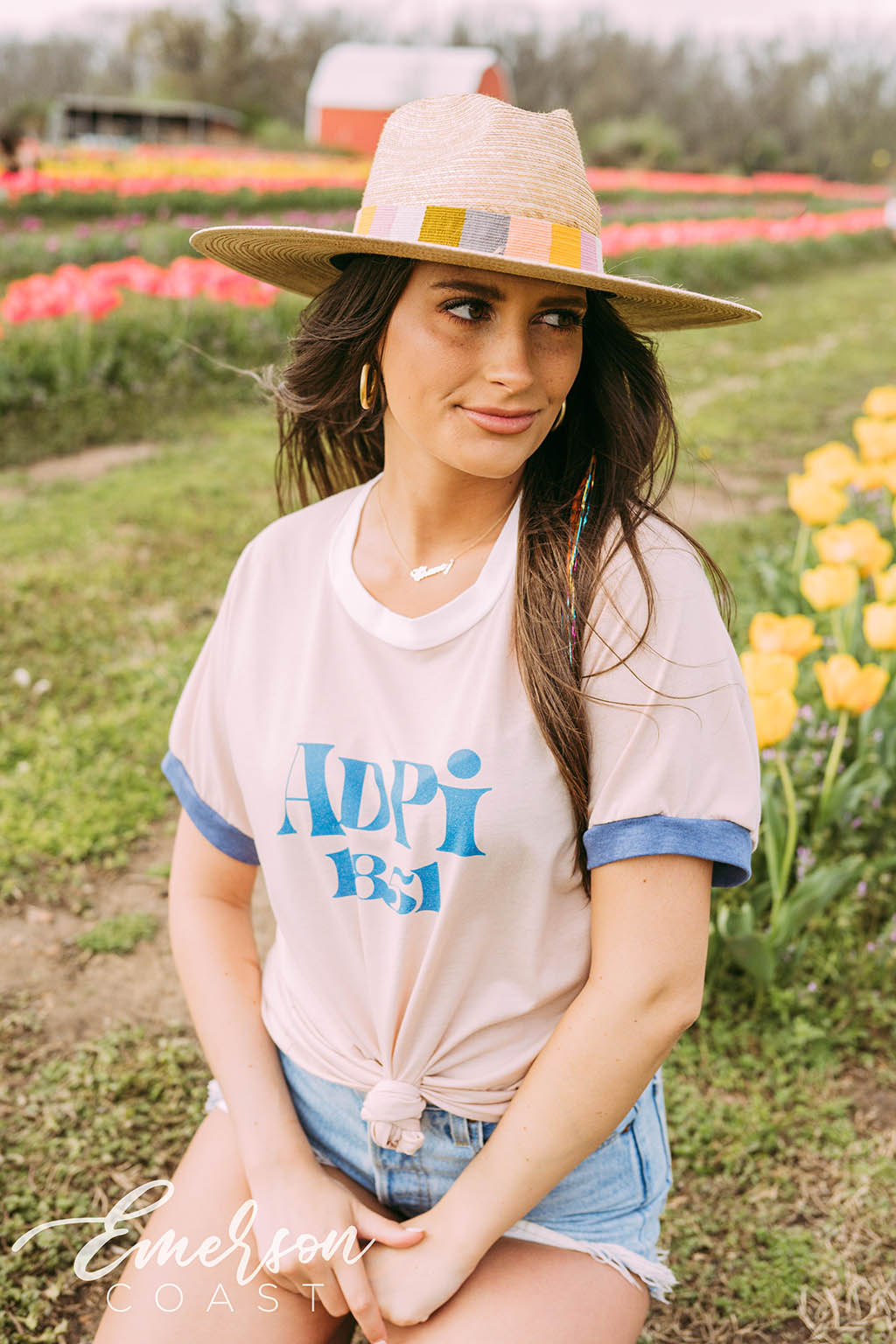 Girl sits in tulip field wearing a white ADPi 1851 ringer tshirt.