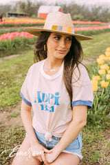Girl sits in tulip field wearing a white ADPi 1851 ringer tshirt.